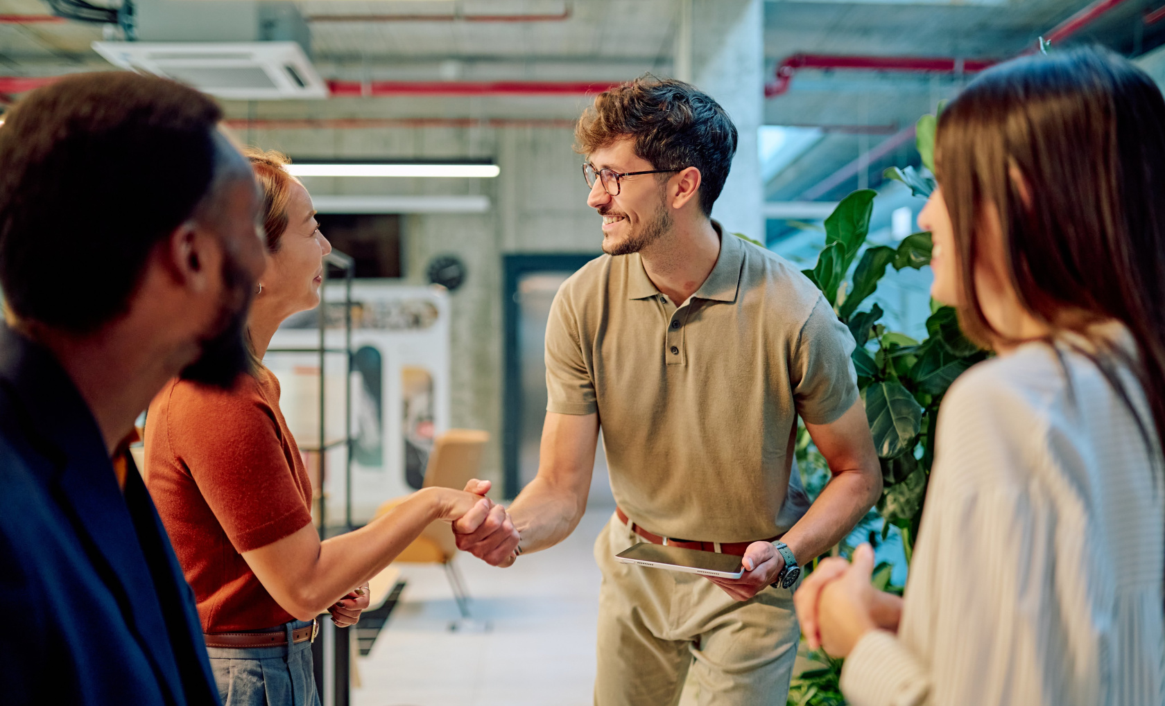 Two colleagues shaking hands in a bright open-plan office while two others look on