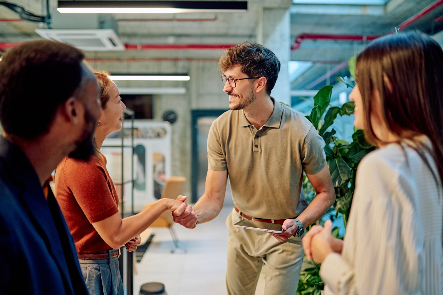 Two colleagues shaking hands in a bright open-plan office while two others look on