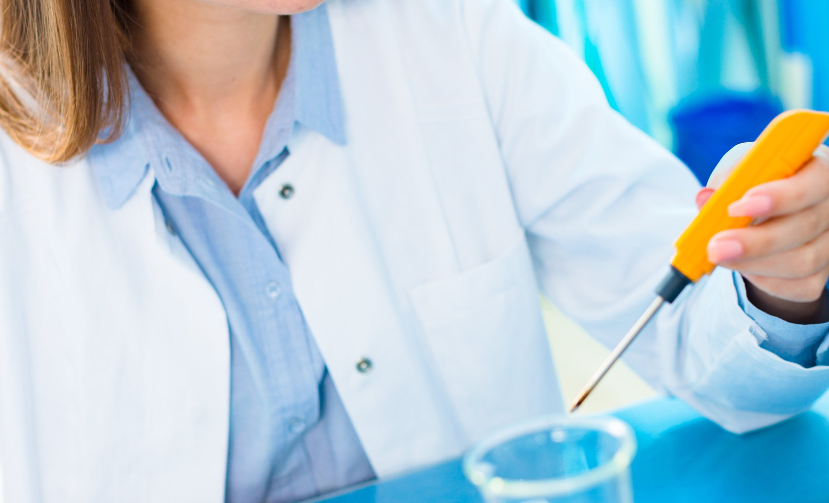A researcher in a lab coat taking notes beside a microscope and a flask in a laboratory