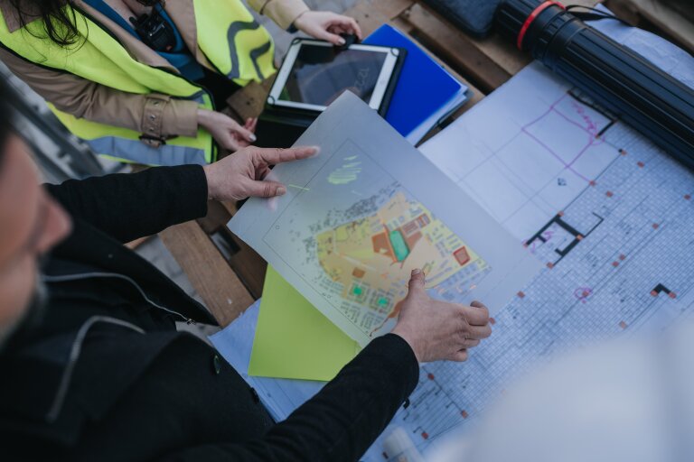 Construction workers in high-visibility vests studying a site plan and technical drawings on a table